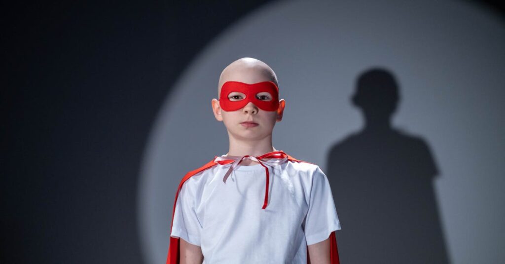 Portrait of young superhero in a white shirt, red cape, and mask with a bold shadow behind.