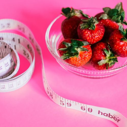 A glass bowl of fresh strawberries paired with a pink measuring tape symbolizes healthy eating.