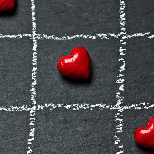 Tic tac toe board on black surface with red heart shapes symbolizing love and connection.