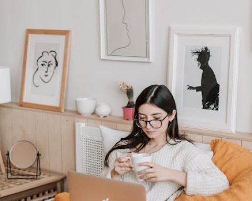 pexels-photo-4050389-4050389 A woman relaxing in bed with coffee and laptop, surrounded by art and comfort.
